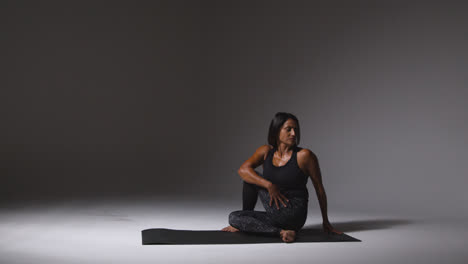 Wide-Angle-Studio-Shot-Of-Mature-Woman-Wearing-Gym-Fitness-Clothing-Sitting-On-Floor-Doing-Pilates-Stretching-Exercises